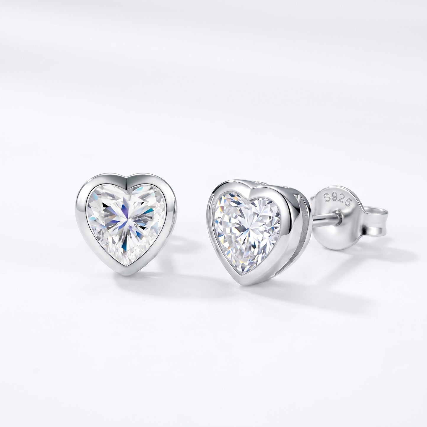 A pair of solid 925 sterling silver low-profile geometric bezel setting heart studs shown from a sharp side-angle view.