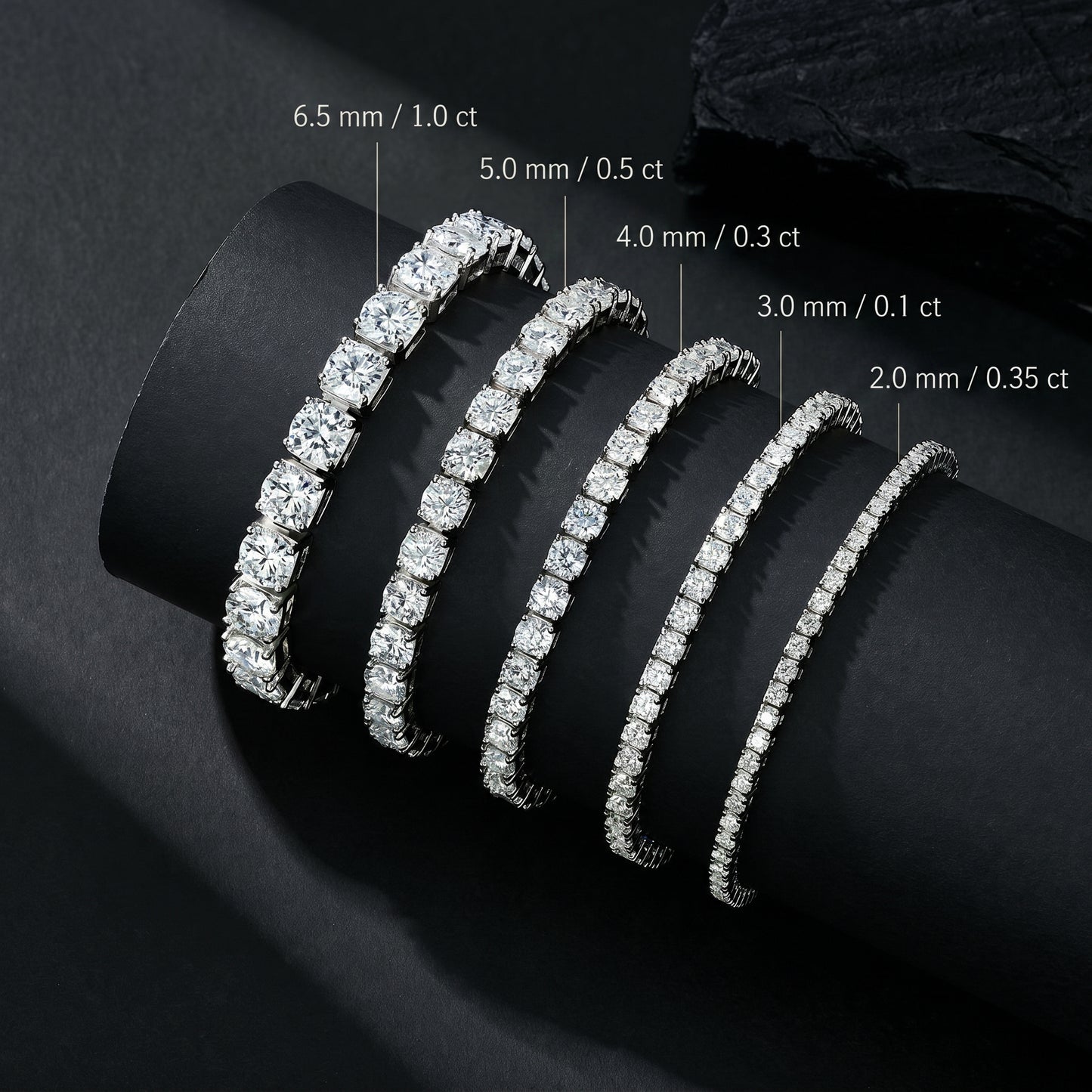 Size comparison chart of Luvia moissanite tennis bracelets ranging from 2.0mm to 6.5mm displayed on a black cylindrical prop.