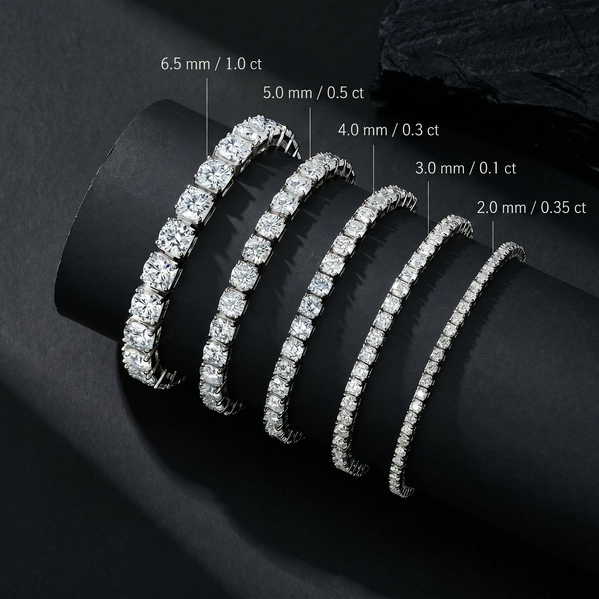 Size comparison chart of Luvia moissanite tennis bracelets ranging from 2.0mm to 6.5mm displayed on a black cylindrical prop.