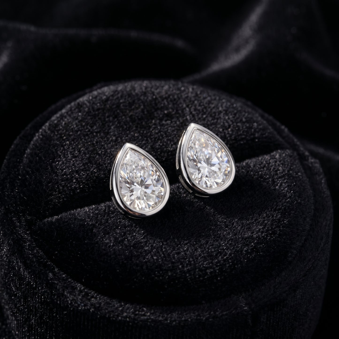 A pair of geometric bezel setting pear moissanite studs perfectly displayed inside a premium black velvet jewelry box.
