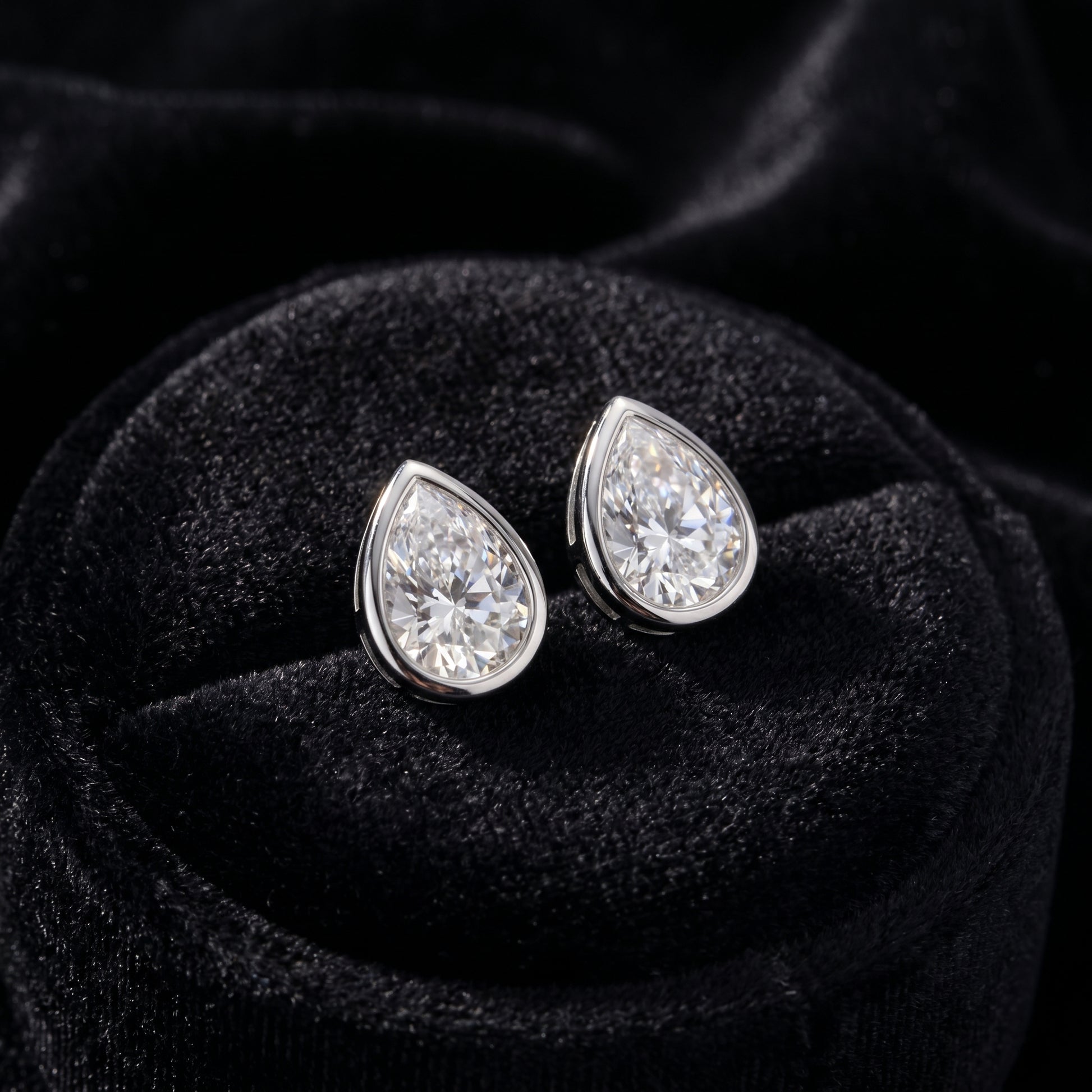 A pair of geometric bezel setting pear moissanite studs perfectly displayed inside a premium black velvet jewelry box.