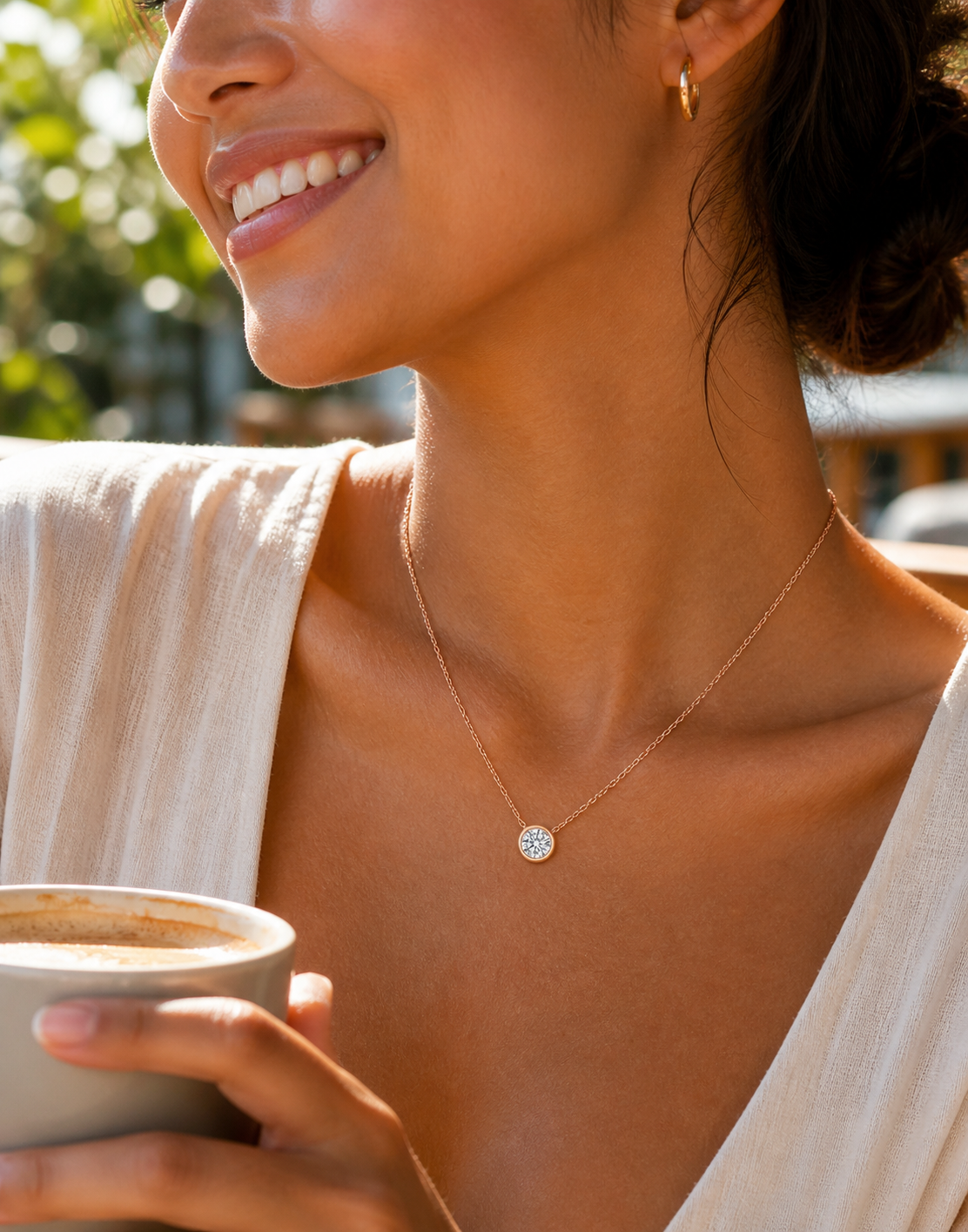 Woman wearing a dainty silver moissanite necklace while holding coffee outdoors