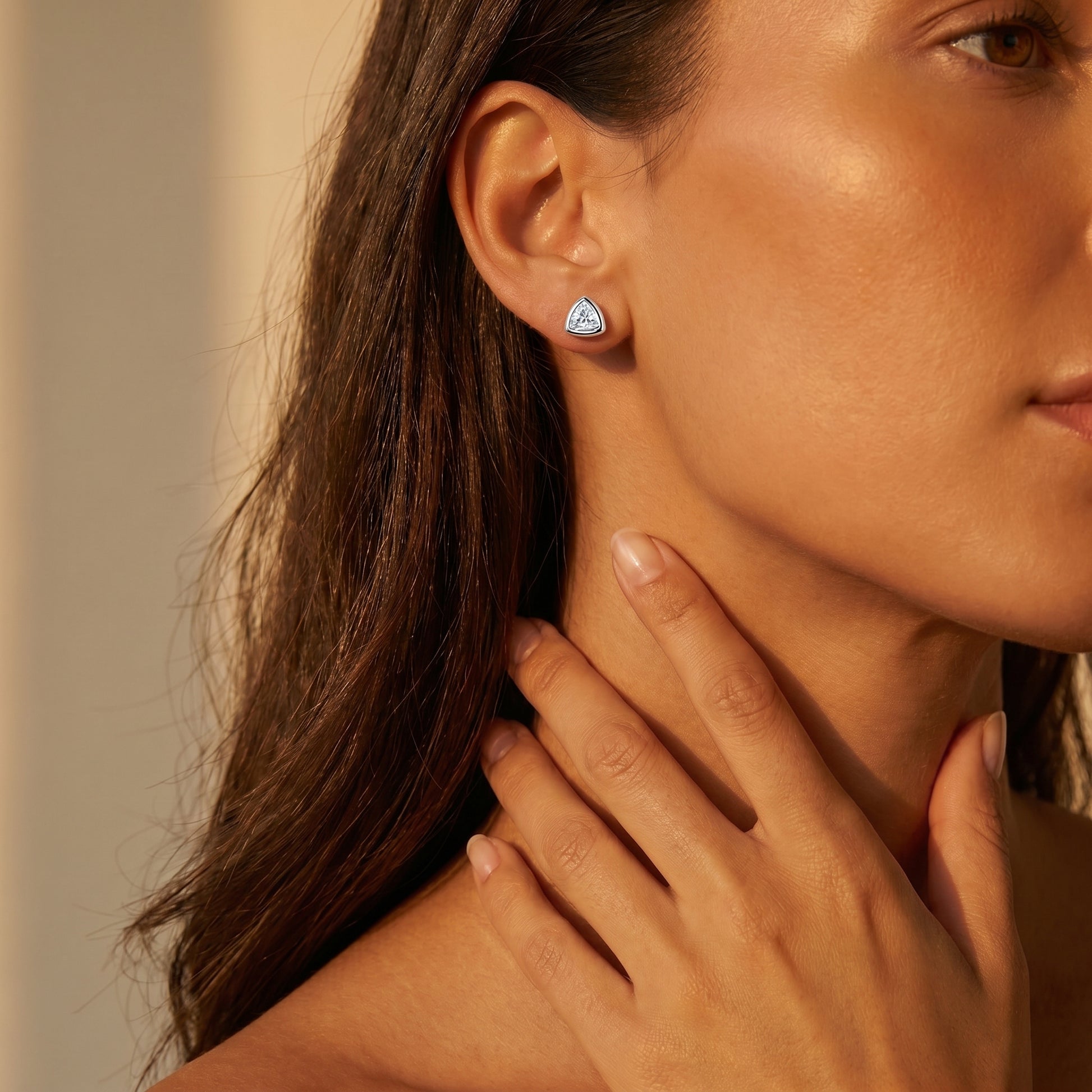 Sleek on-ear lifestyle look of Luvia geometric trillion moissanite stud earrings displayed on a tanned skin tone model.