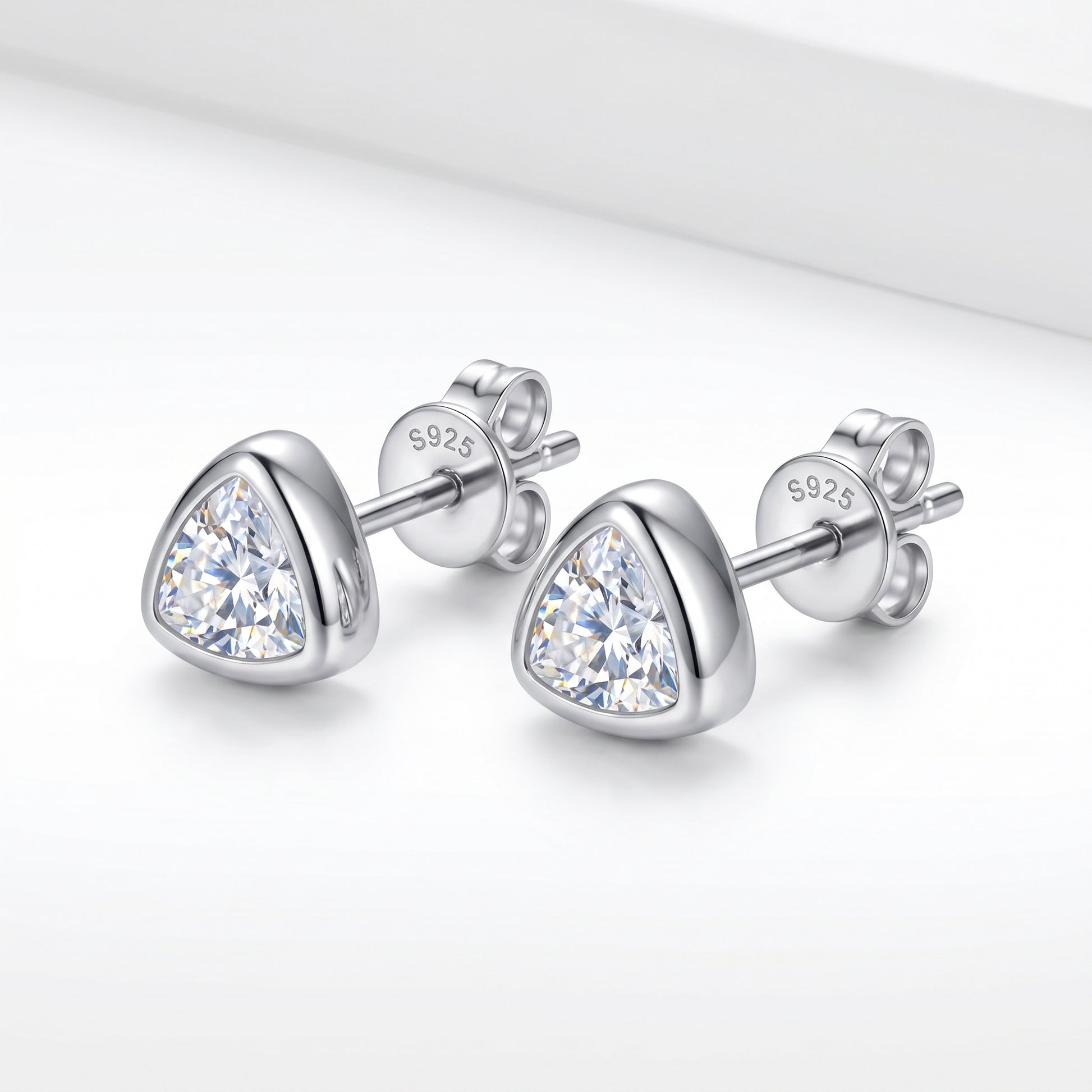 A pair of solid 925 sterling silver low-profile geometric bezel setting moissanite studs shown from a sharp side-angle view.