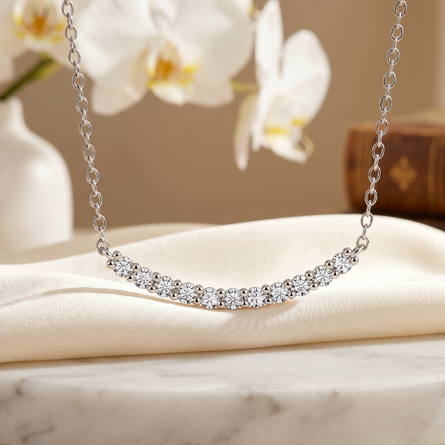 Curved moissanite bar necklace styled with white flowers on soft fabric