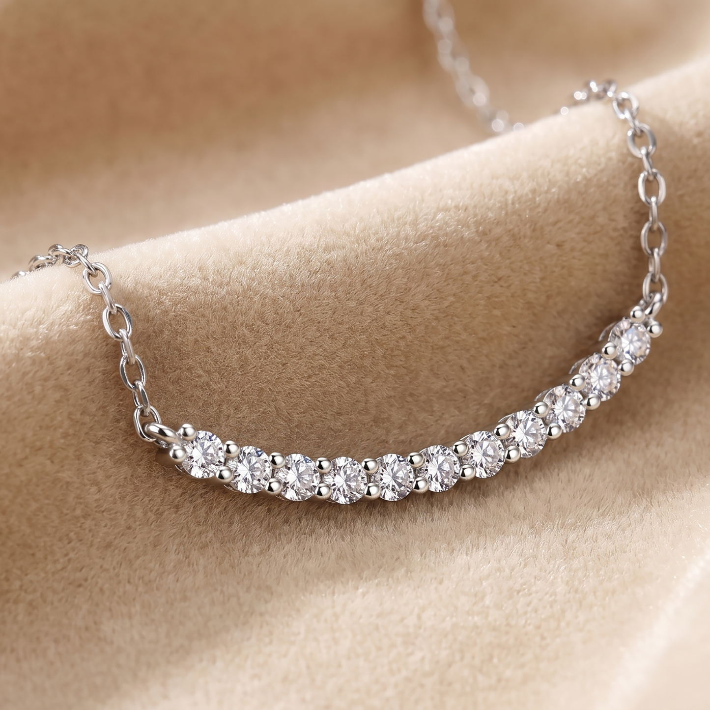 Silver curved moissanite bar necklace resting on beige satin fabric