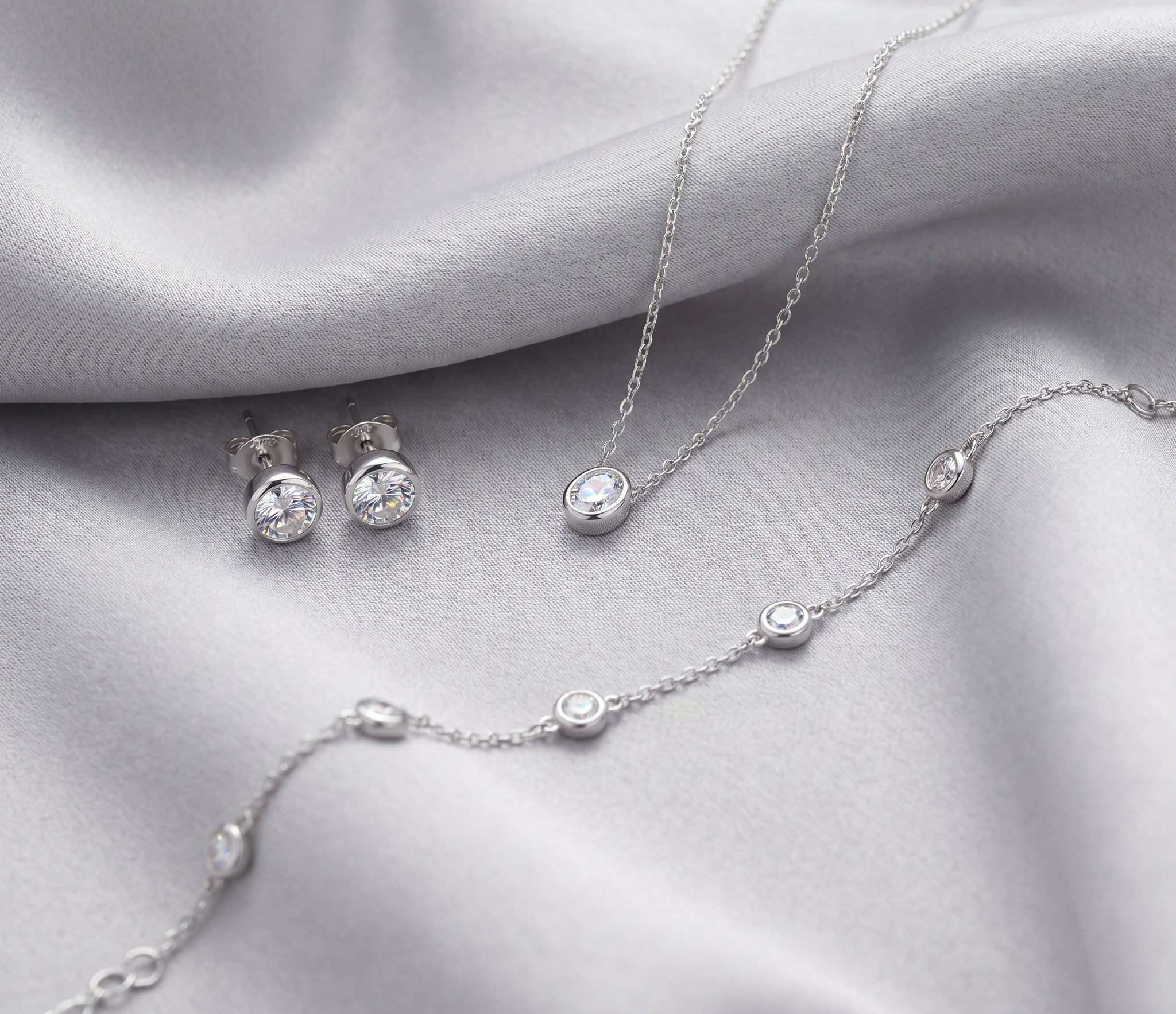 Daily wear moissanite jewelry with sterling silver necklace, earrings, and bracelet on silver silk