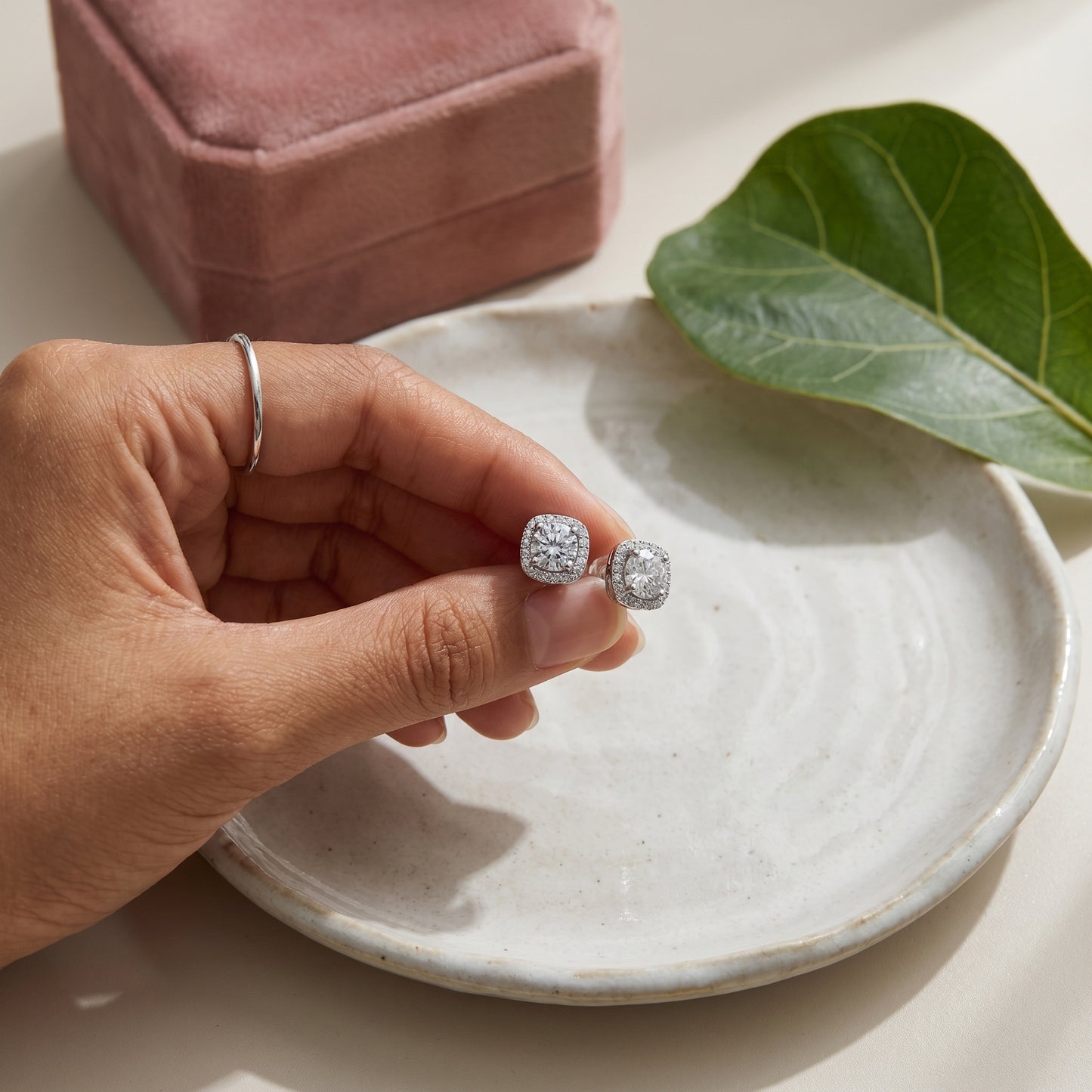 Cushion halo moissanite stud earrings held above a white ceramic tray