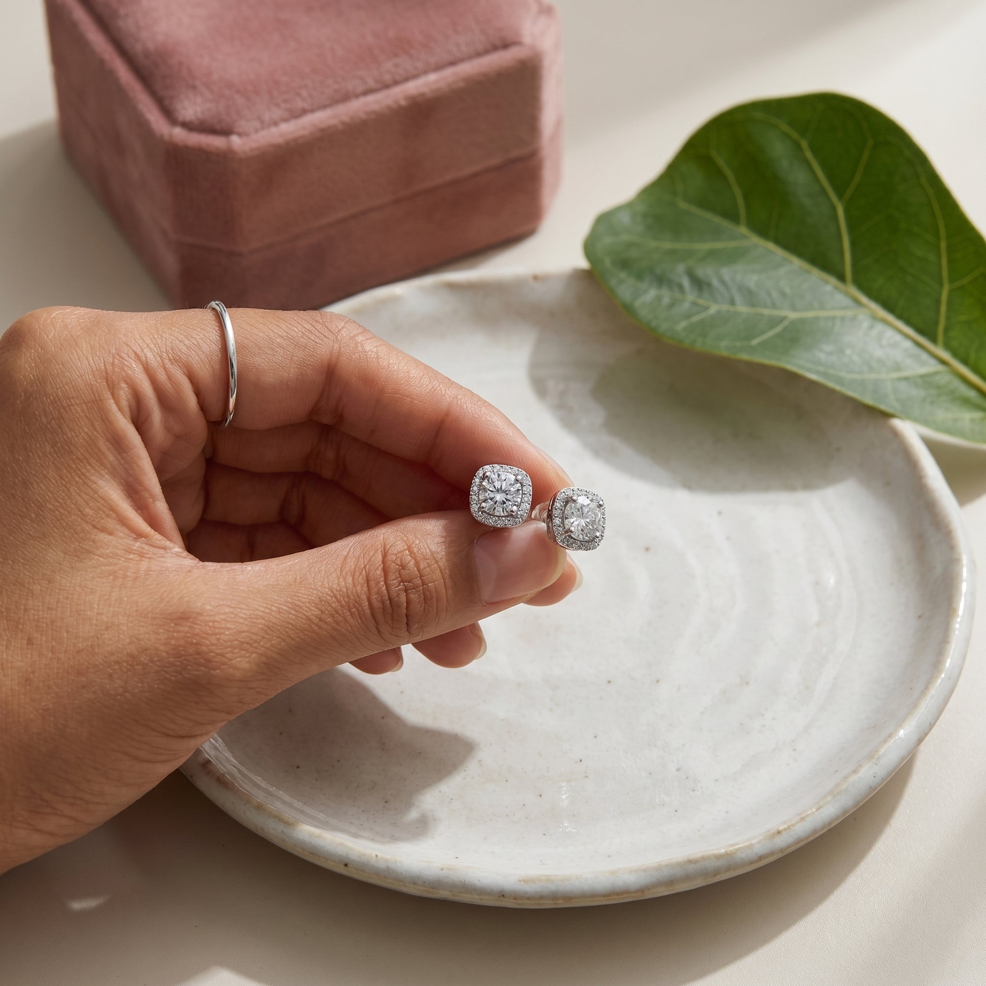Cushion halo moissanite stud earrings held above a white ceramic tray
