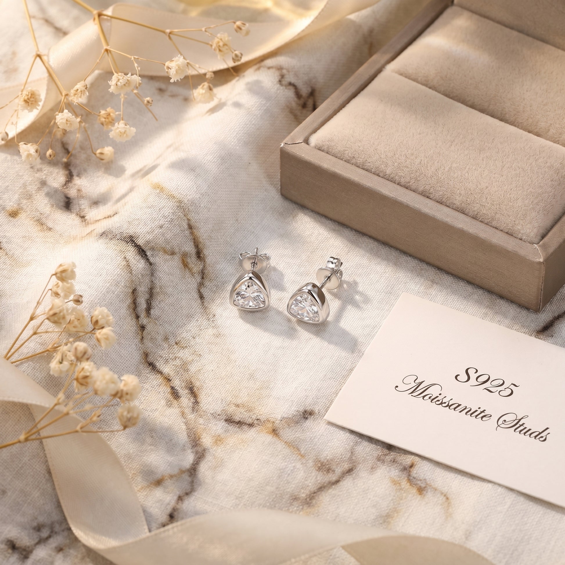 Minimalist architectural trilliant cut moissanite earrings paired with a luxury leather jewelry box in soft warm lighting.
