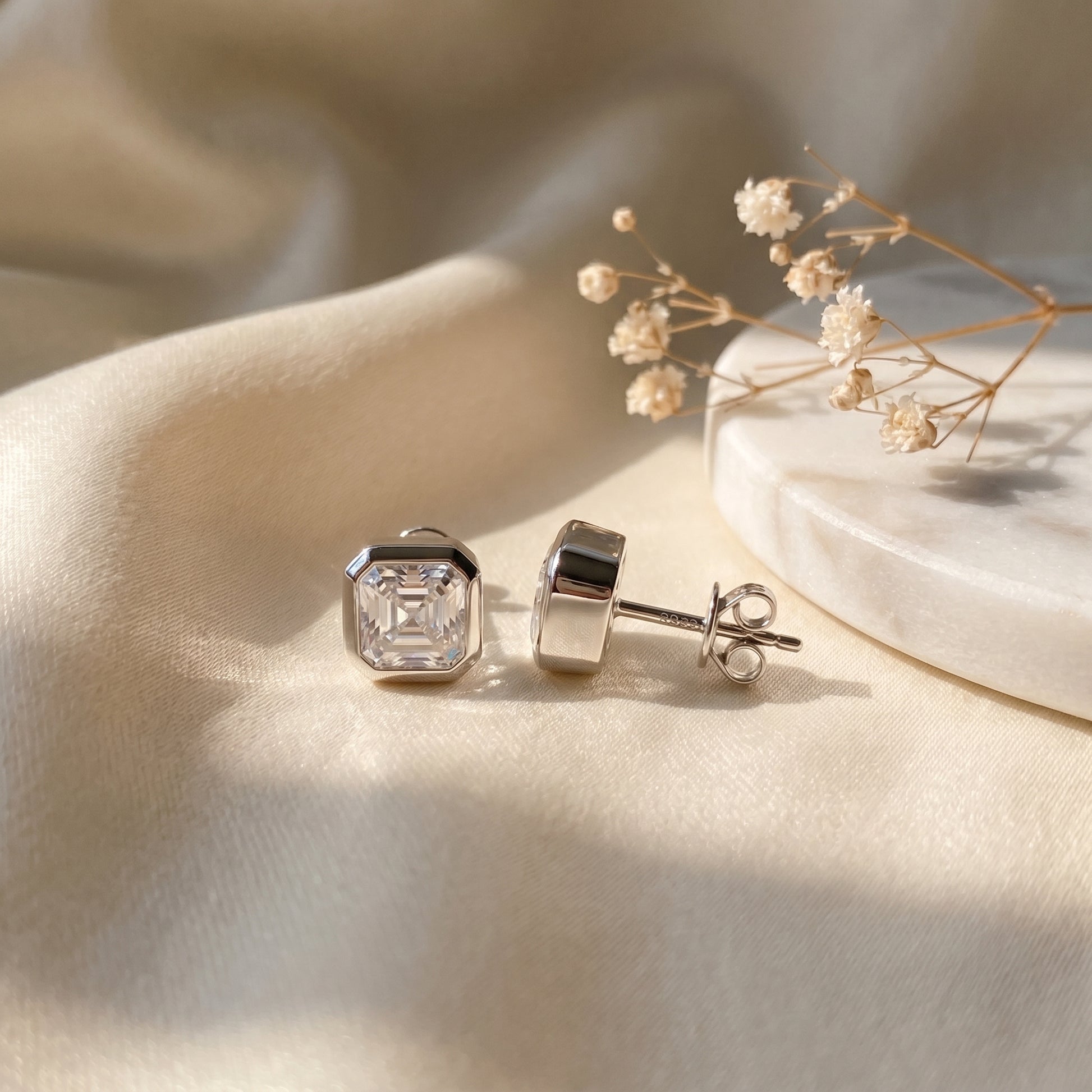 A pair of solid 925 sterling silver low-profile geometric bezel setting Asscher studs showcased under soft, elegant lighting.
