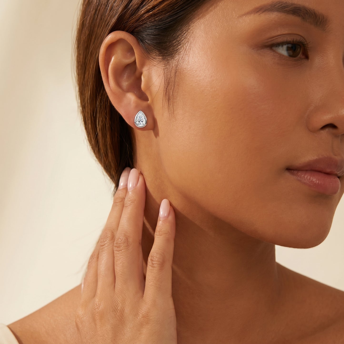 Sleek on-ear lifestyle look of Luvia elegant pear shape moissanite stud earrings displayed on a tanned skin tone model.
