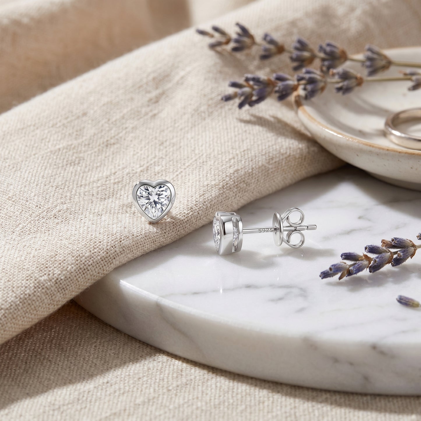 Minimalist heart cut moissanite studs beautifully laid on a textured linen background with elegant dried lavender accents.