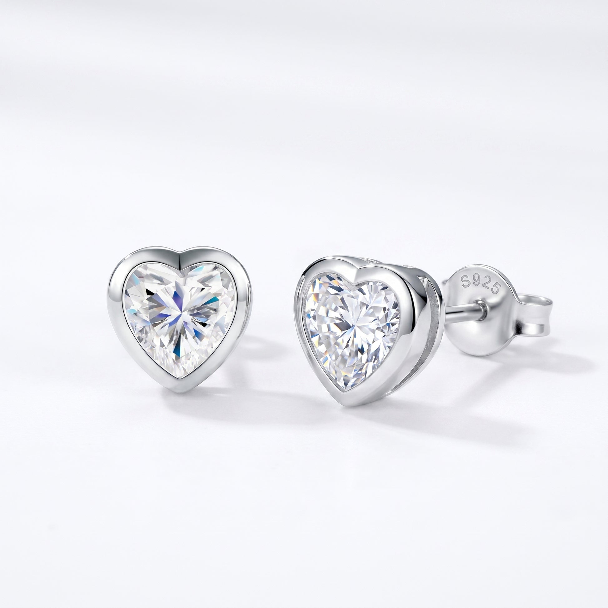 A pair of solid 925 sterling silver low-profile geometric bezel setting heart studs shown from a sharp side-angle view.